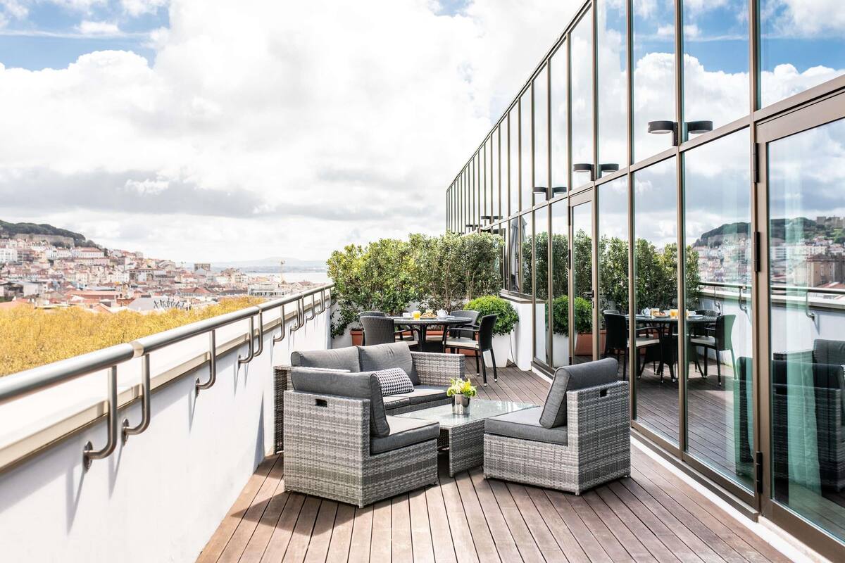 Un balcón con mobiliario de mimbre, una mesa y sillas, con vistas a un paisaje urbano.