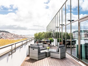 Un balcón con mobiliario de mimbre, una mesa y sillas, con vistas a un paisaje urbano.