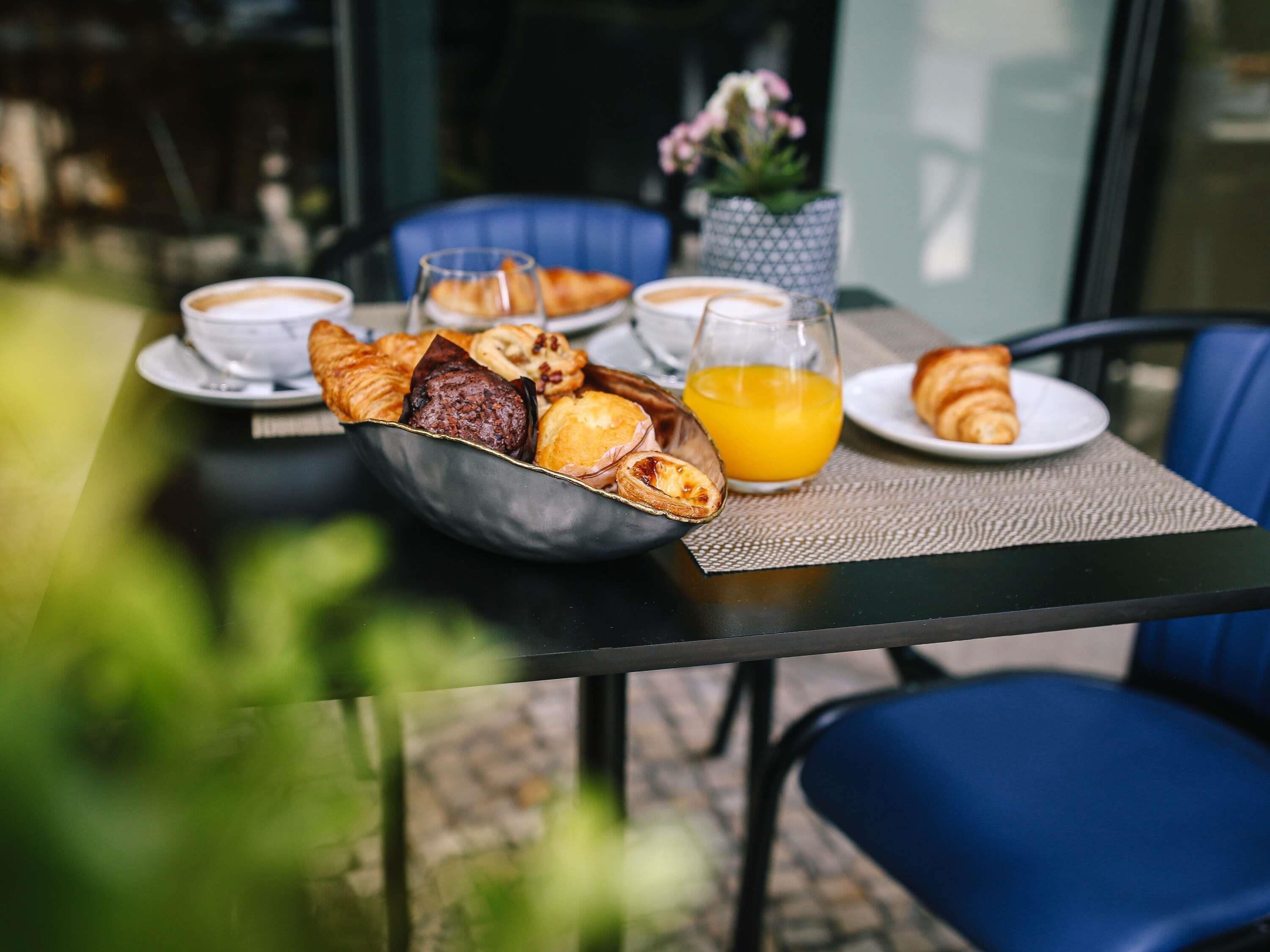 Une table de petit-déjeuner avec des croissants, des viennoiseries, du café et du jus d’orange.