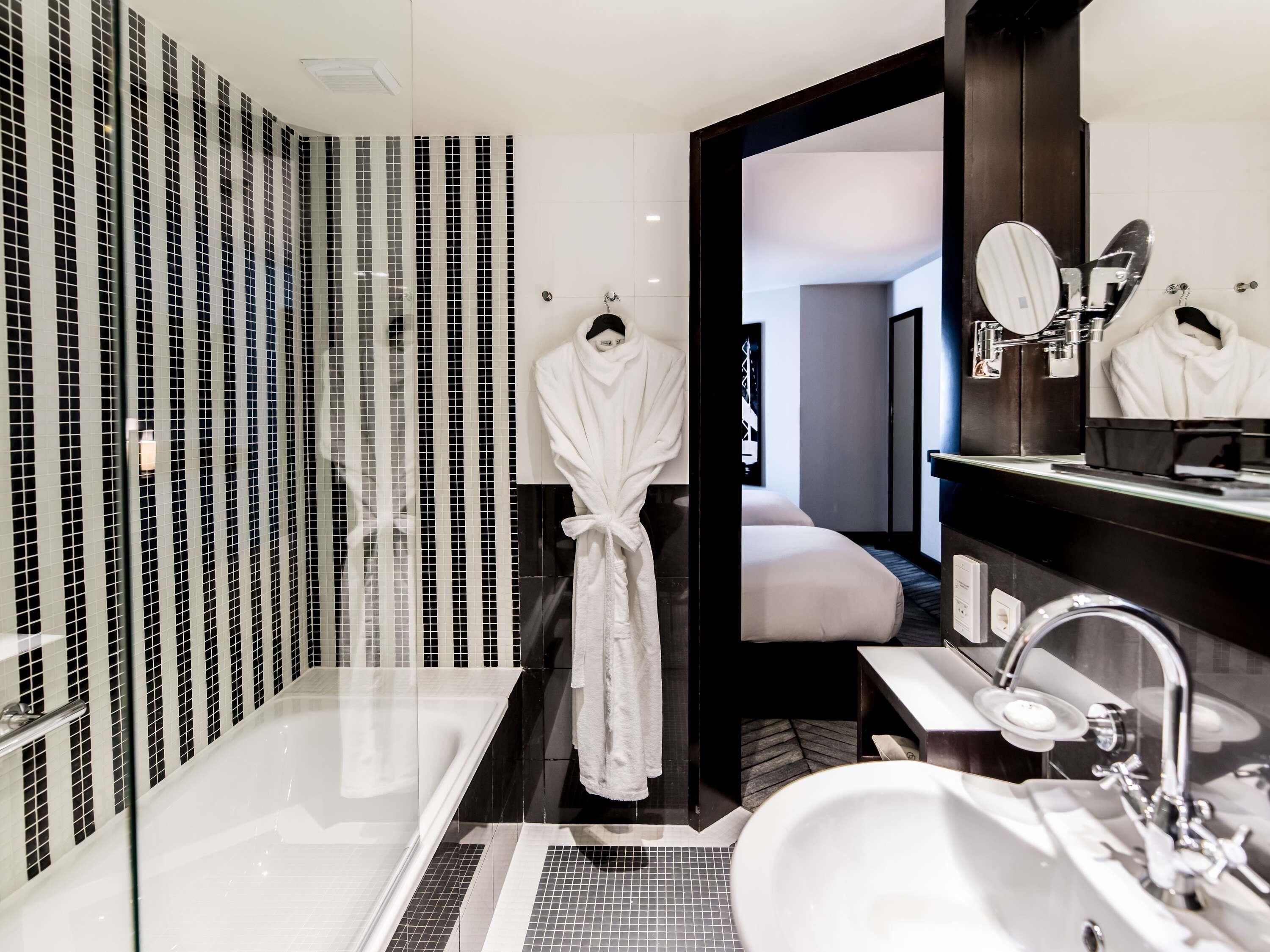 Un baño moderno con ducha de vidrio, un espejo grande y una bata blanca colgada en un perchero.
