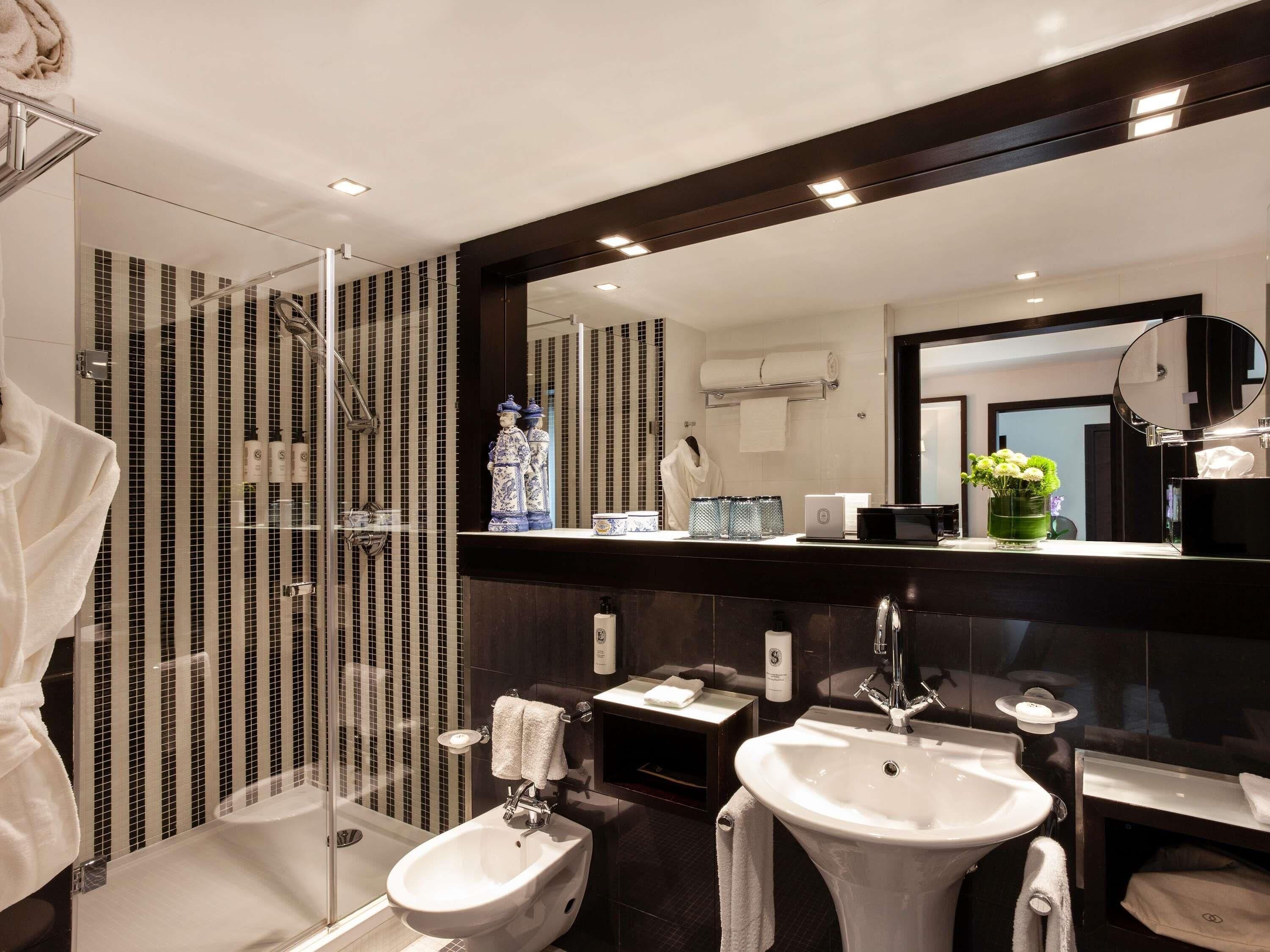Une salle de bain moderne équipée d’une douche, d’un bidet, de deux lavabos, d’un grand miroir et d’un porte-serviettes.