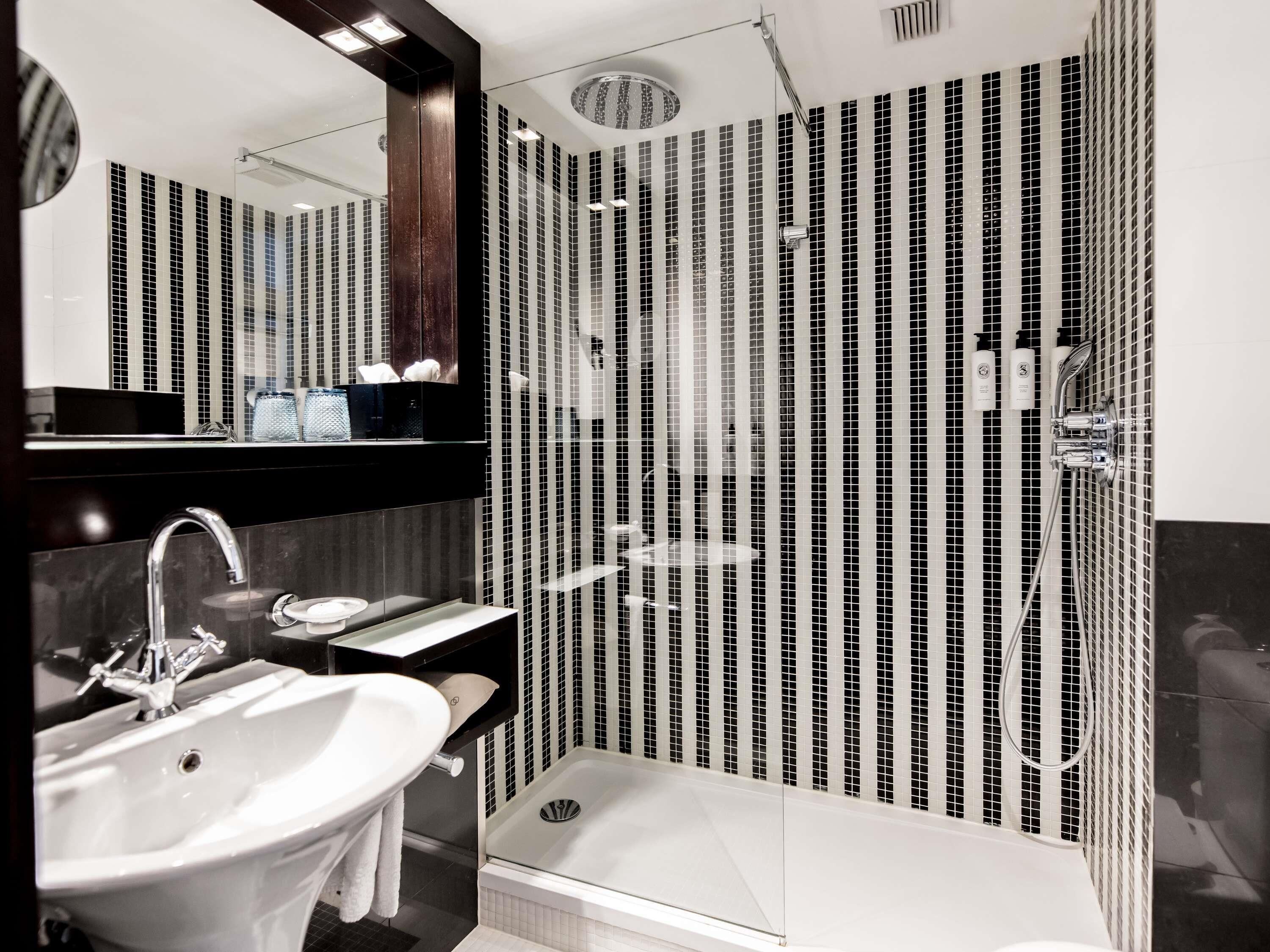 Un baño moderno con un espejo grande, un lavabo, una ducha con mampara de vidrio y pared con azulejos.