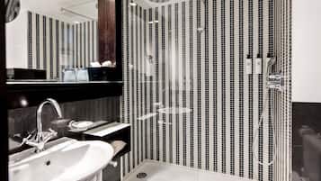 Un baño moderno con un espejo grande, un lavabo, una ducha con mampara de vidrio y pared con azulejos.