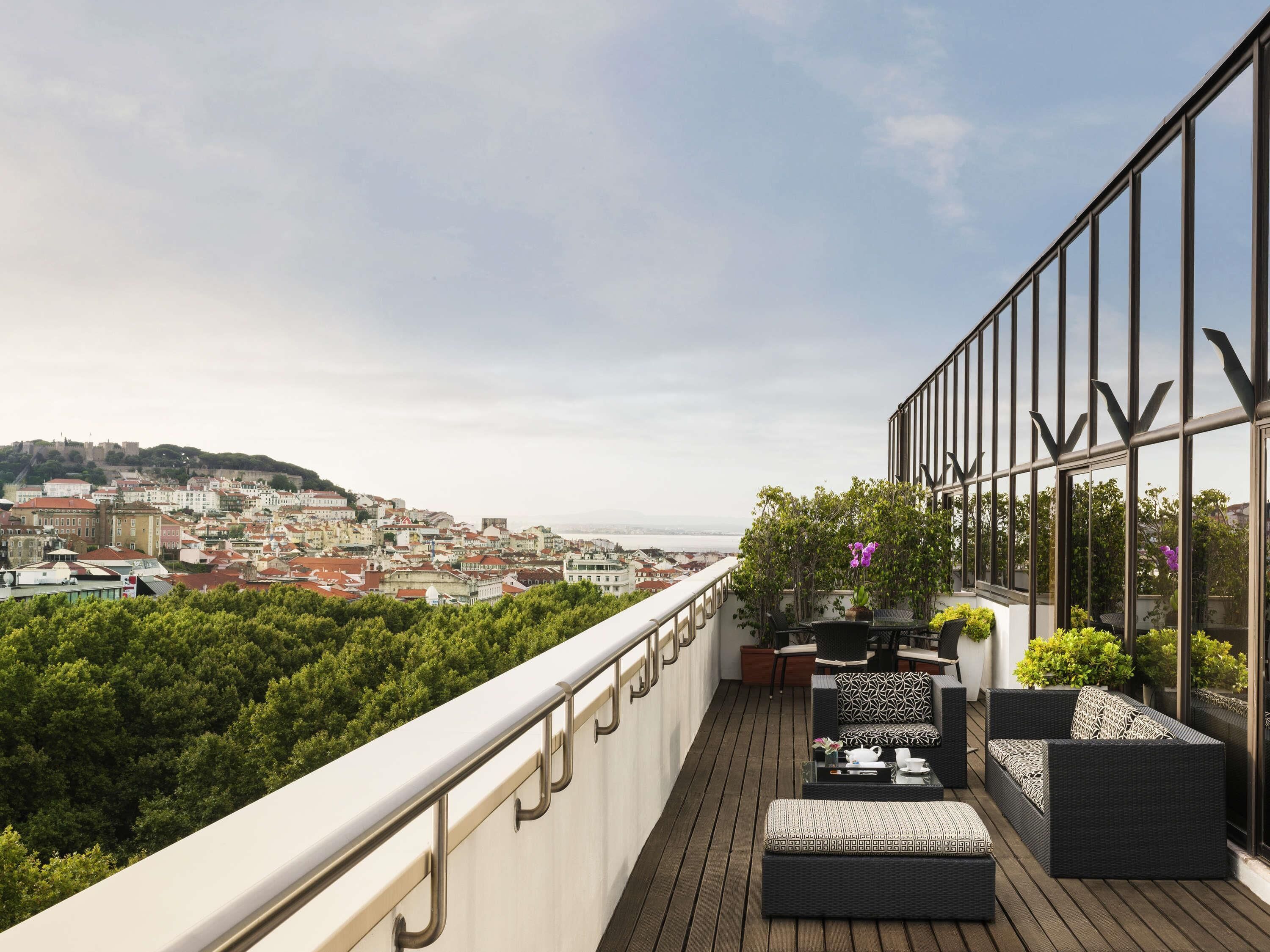 A balcony with a view of a cityscape, furnished with outdoor seating and potted plants.