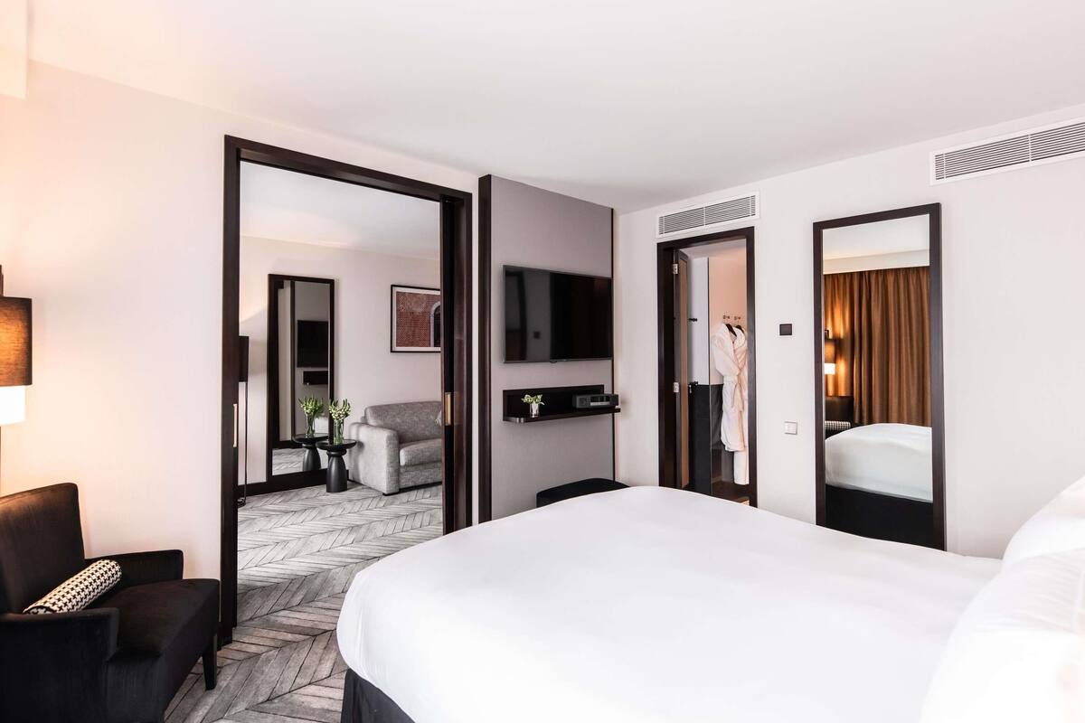 Habitación de hotel con una cama grande, un escritorio con silla, televisión, espejo y armario.
