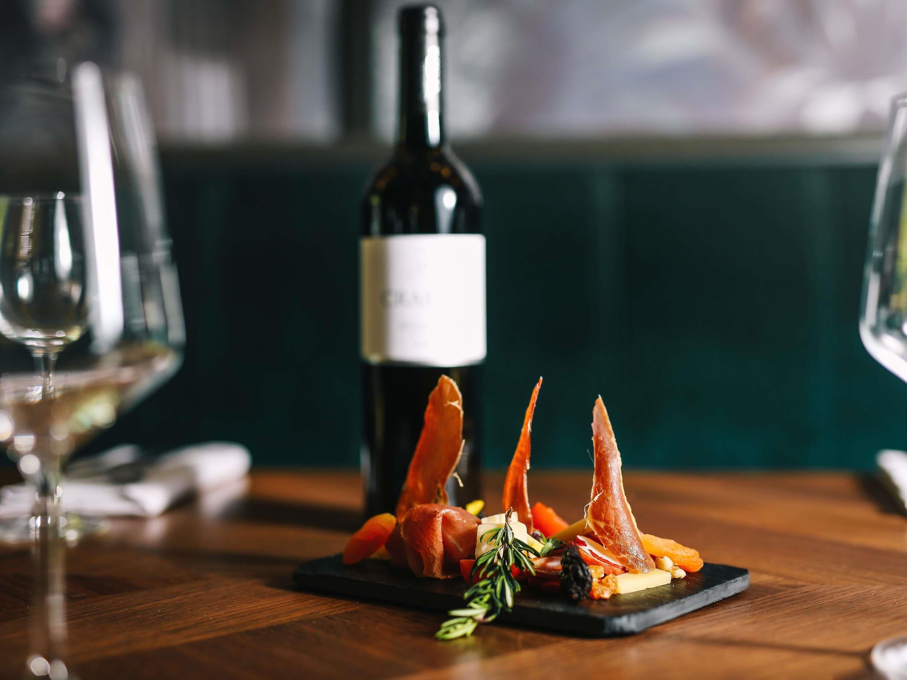 A dining table with a plate of food, a bottle of wine, and two glasses.