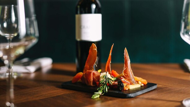 A dining table with a plate of food, a bottle of wine, and two glasses.