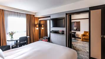 A hotel room with a large bed, a desk with a chair, a TV mounted on the wall, and a view of the hallway.