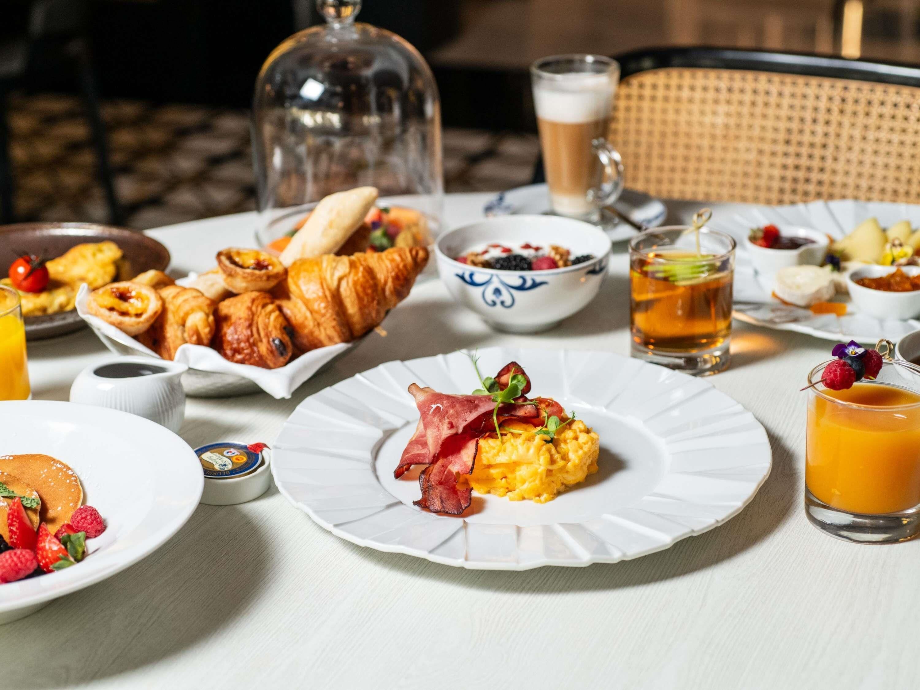 Un desayuno con cruasanes, huevos revueltos y un vaso de zumo de naranja.