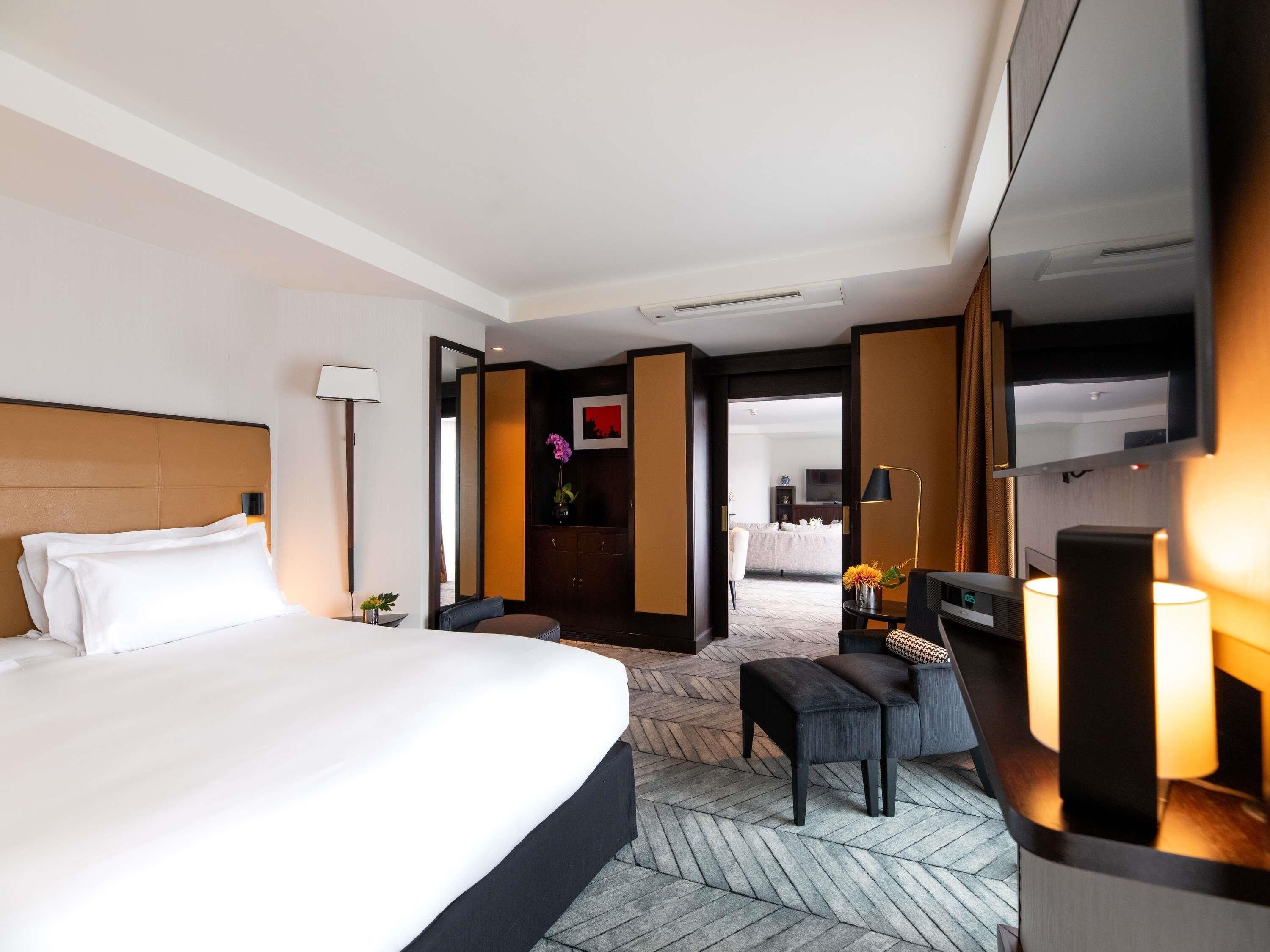 A hotel room with a large bed, a desk with a chair, a TV, and a mirror.