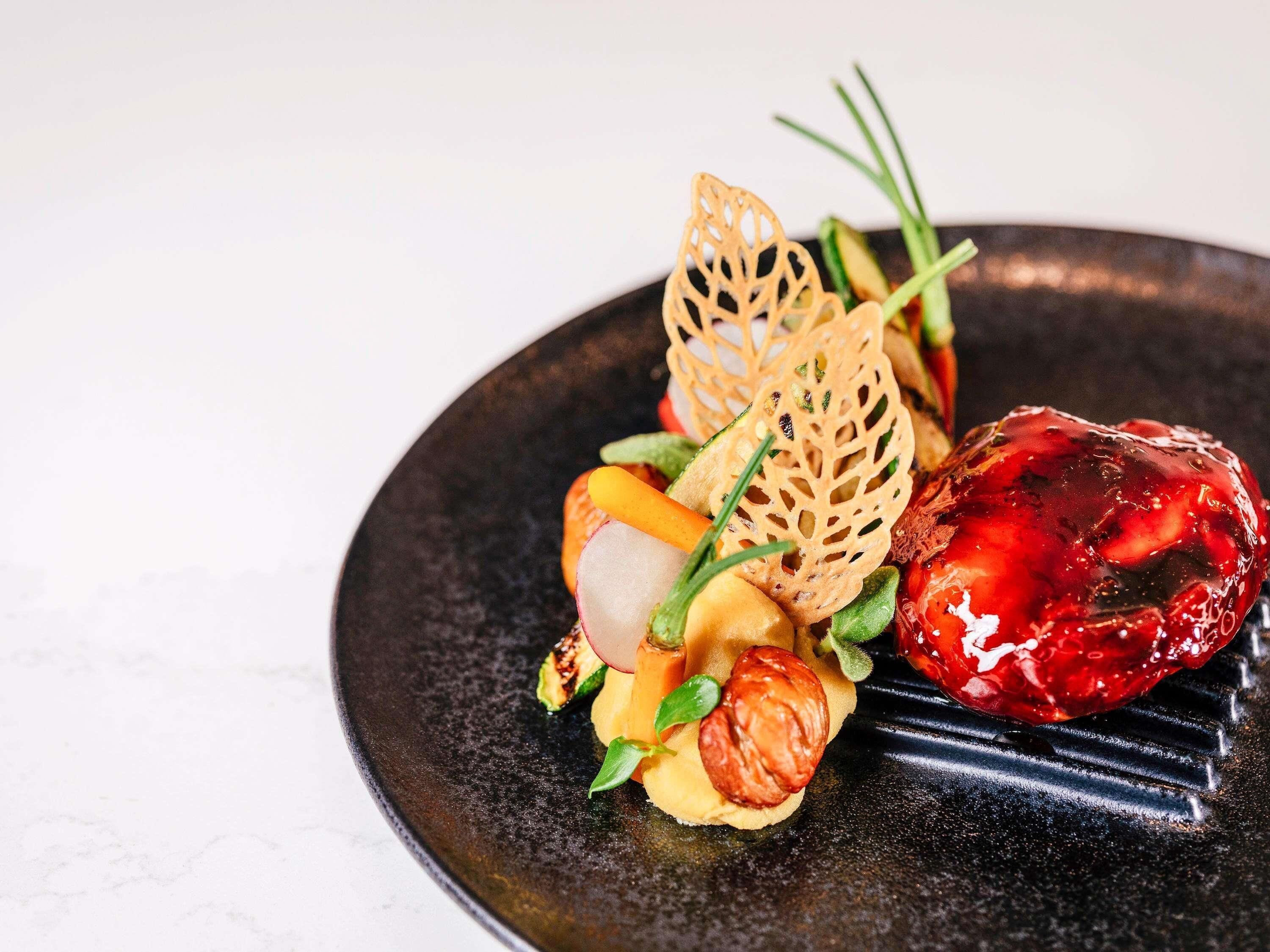 A dish with various vegetables and a decorative element on a dark plate.