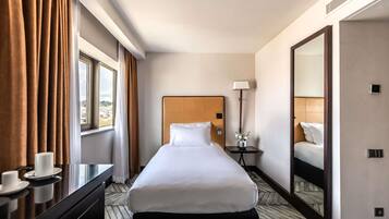 A hotel room with a large bed, a bedside table with a lamp, a mirror, and a view of the city through the window.