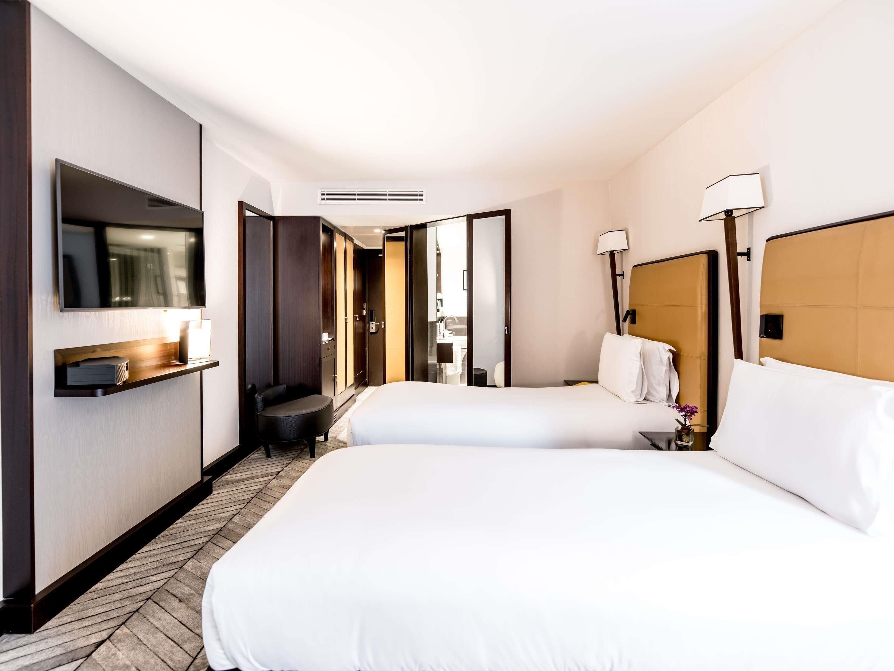 A hotel room with two beds, a TV, a desk, and a wardrobe.