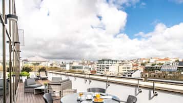 Una terraza en la azotea con mobiliario exterior, una mesa con desayuno y vistas a la ciudad.