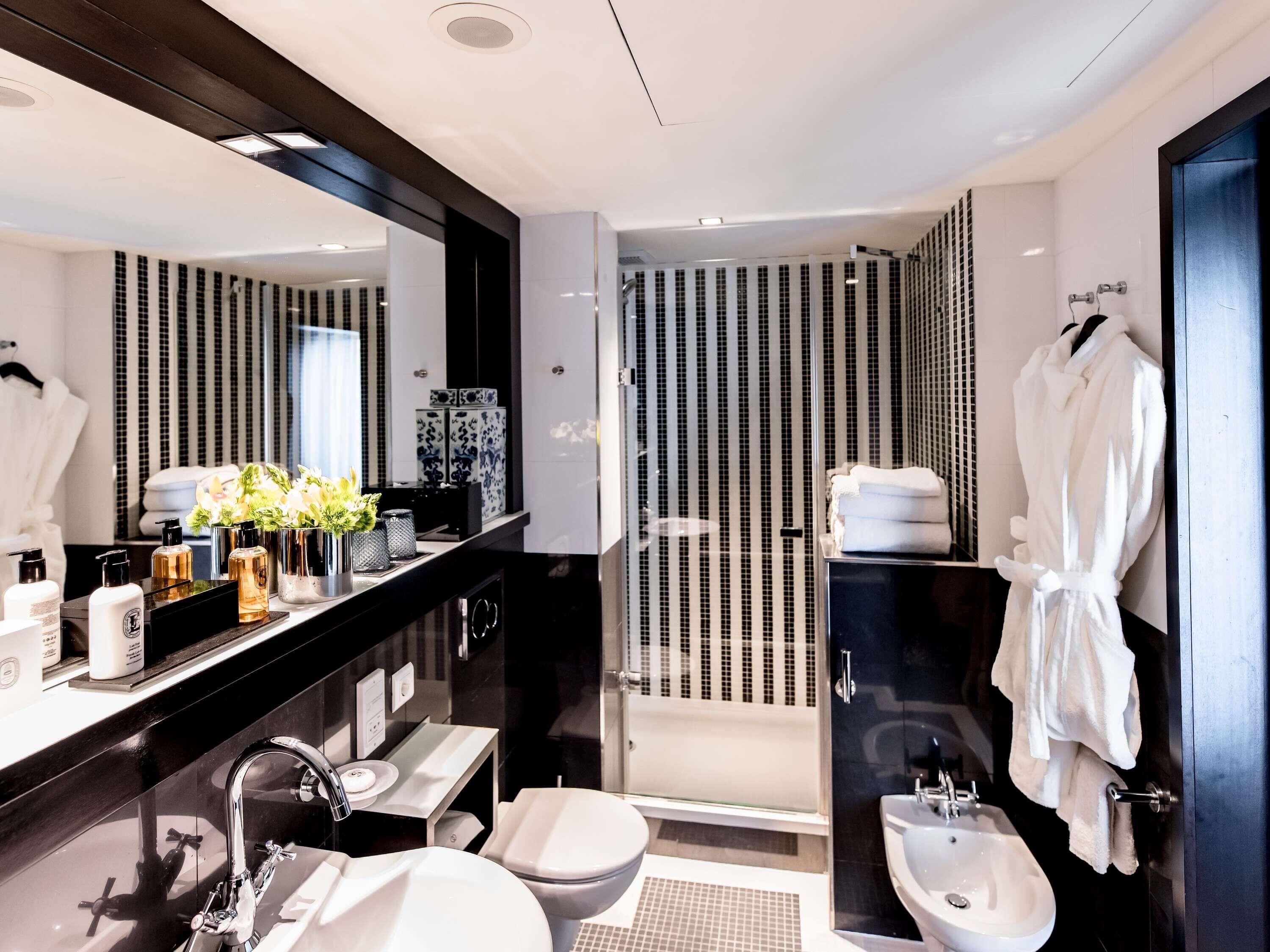 Een moderne badkamer met een grote spiegel, een wastafel met toiletartikelen, een hygiëneslot en een ruime douche.