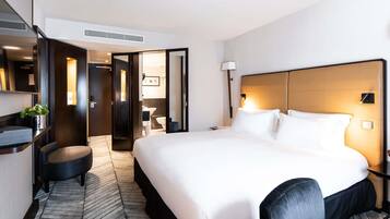 A hotel room with a large bed, a desk with a chair, a mirror, and a bathroom visible through an open door.