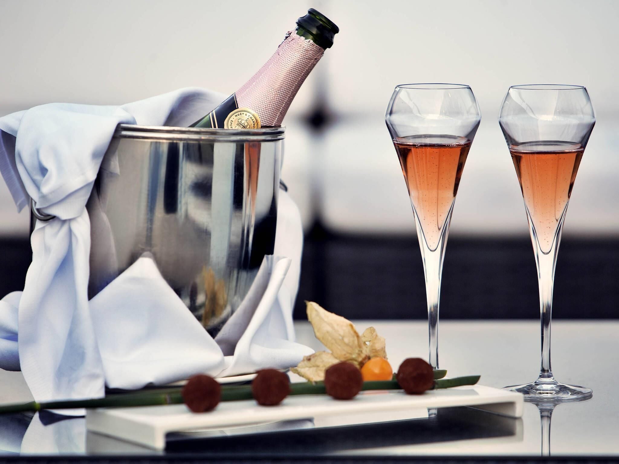 Une bouteille de champagne dans un seau en métal, deux coupes de champagne et quelques éléments décoratifs sur une table.