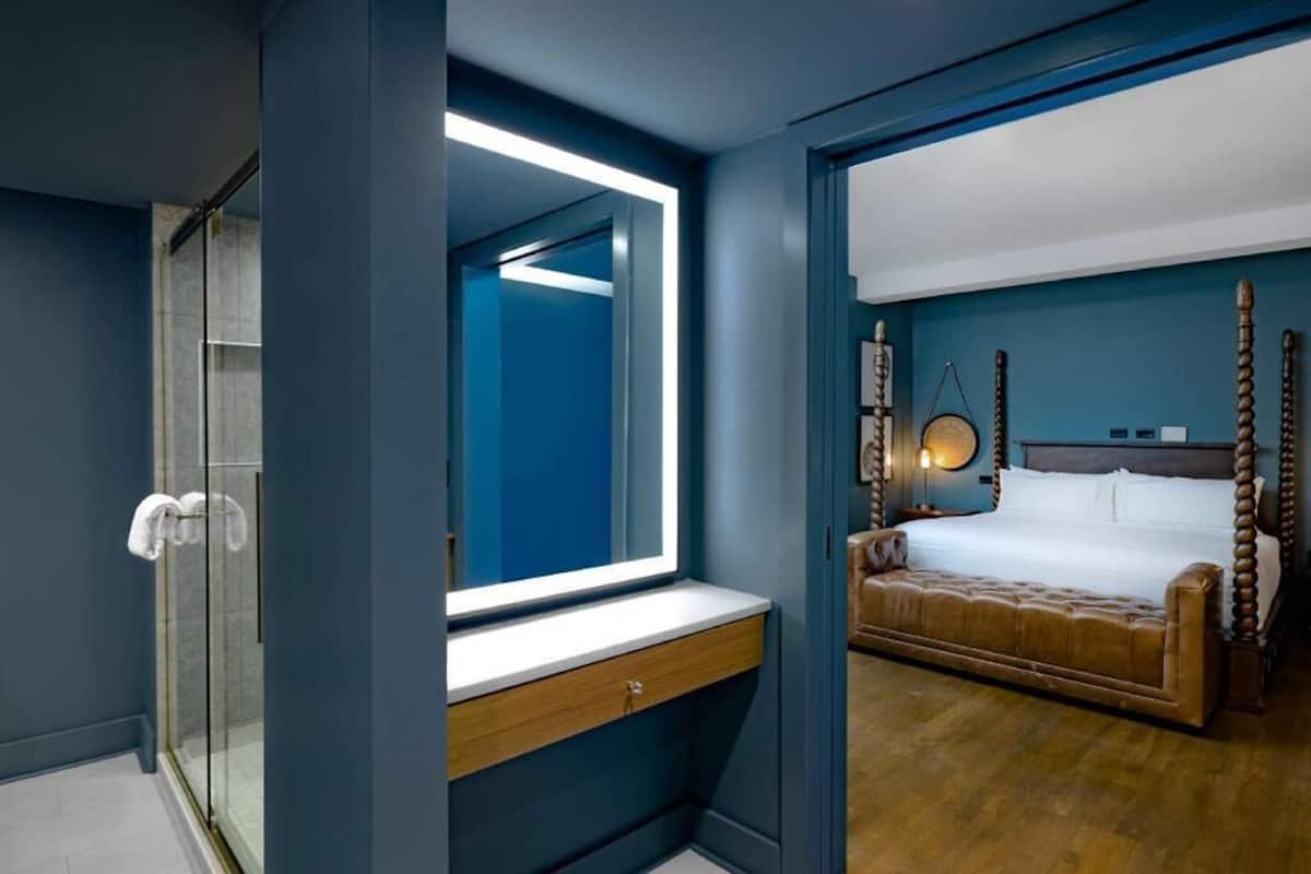 A modern bedroom with a large mirror, a wooden bedside table, a four-poster bed, and a glass shower enclosure.