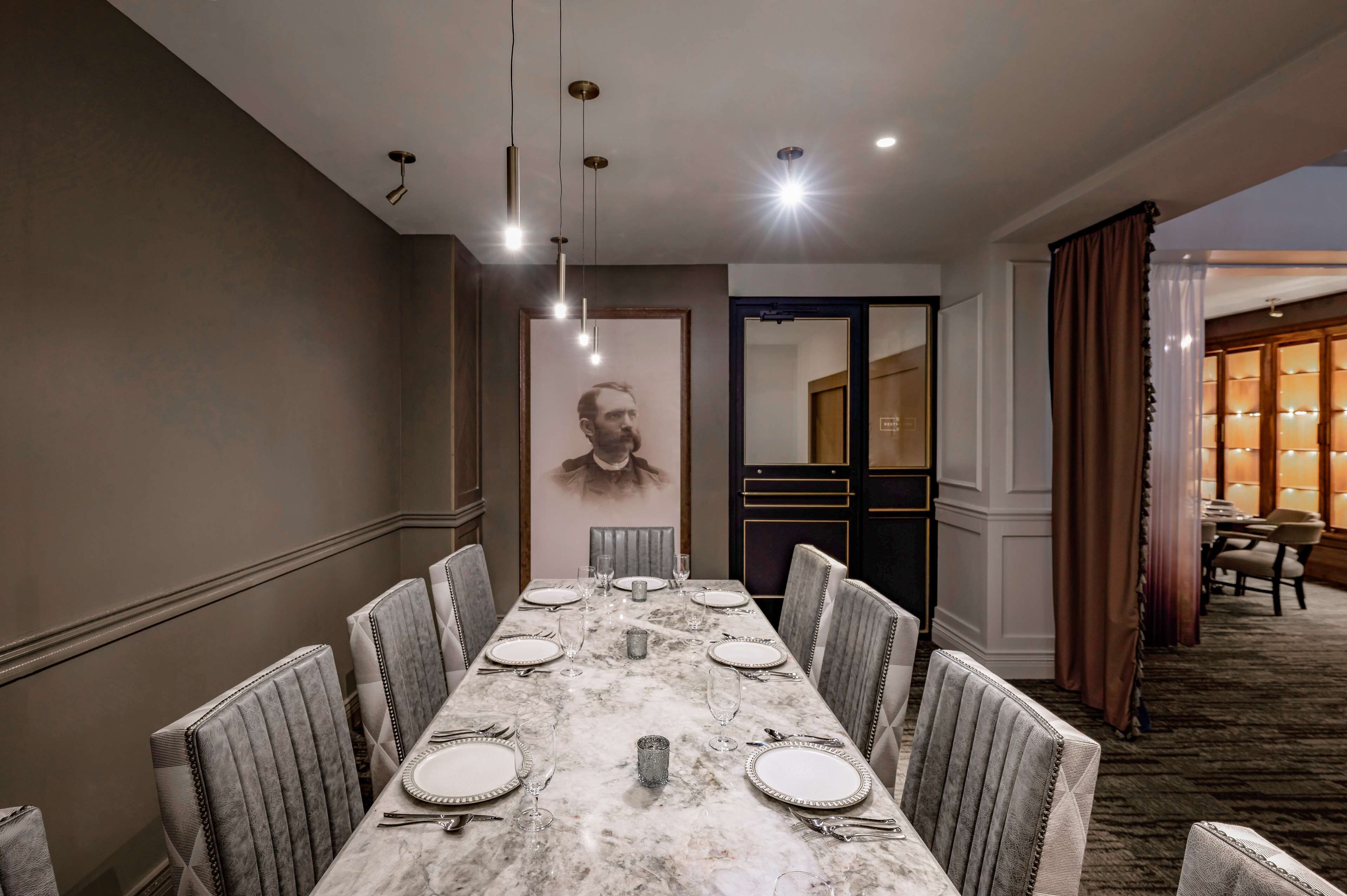 A dining area with a marble table, upholstered chairs, and pendant lighting.