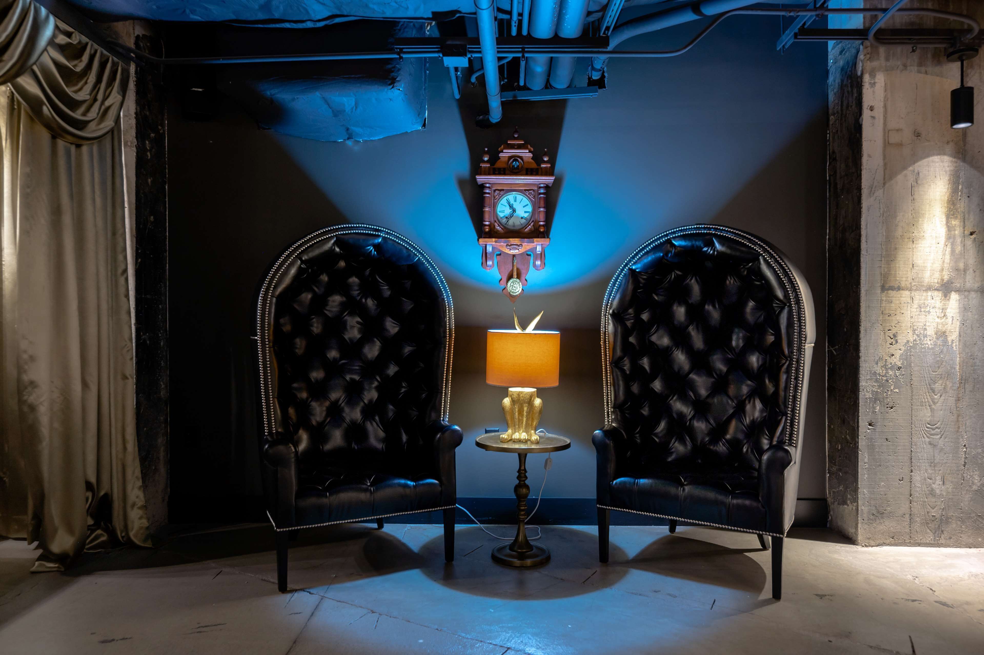 A room with two black leather armchairs, a small round table with a lamp, and a hanging wooden clock.