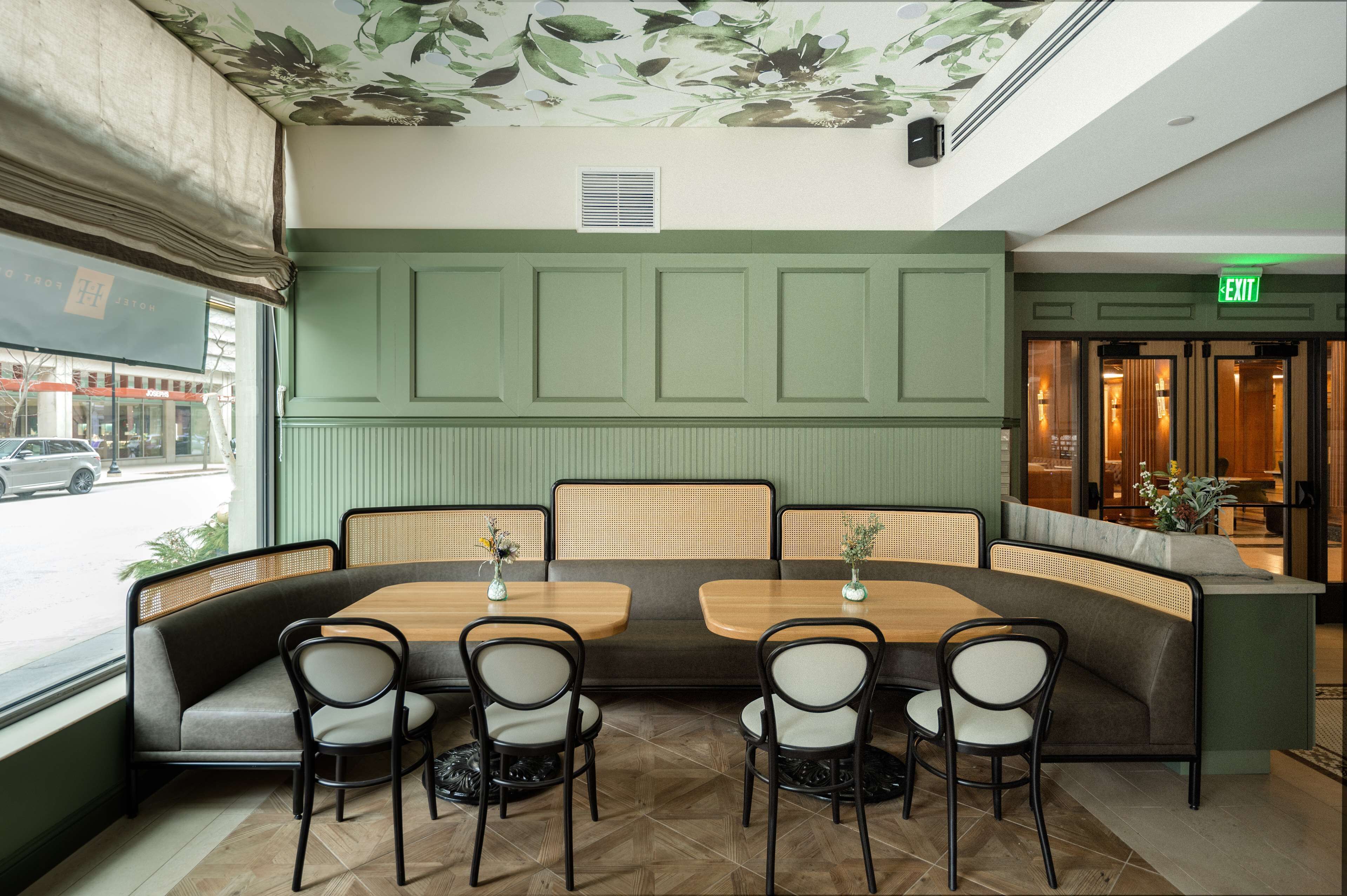 Un restaurante con pared verde, mesas de madera y asientos acolchados.