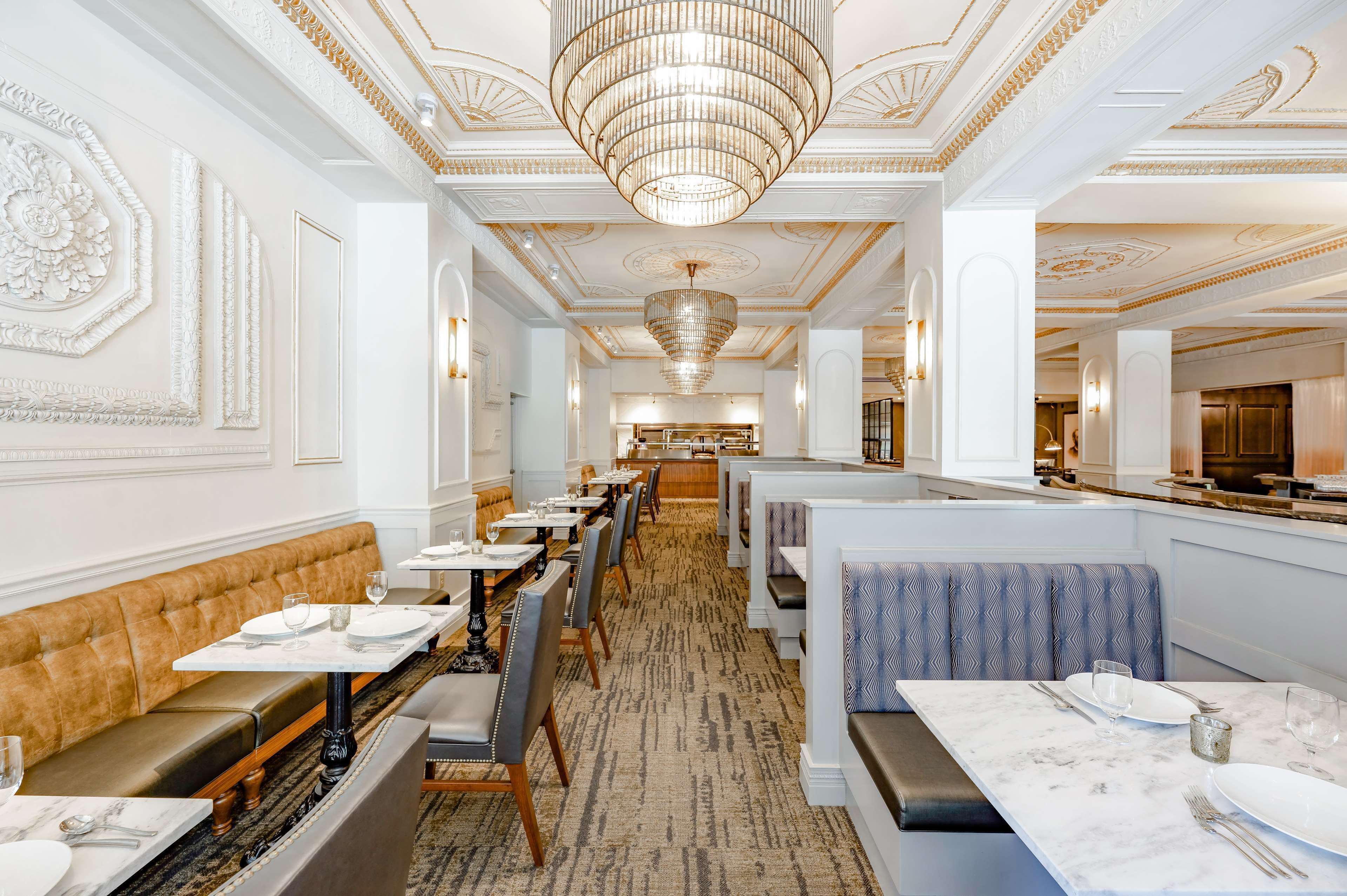 A restaurant with a long, elegant interior featuring high ceilings, chandeliers, and ornate wall decorations.