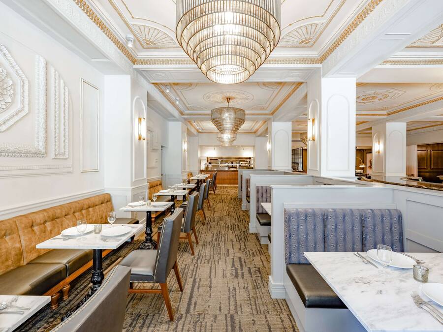 A restaurant with a long, elegant interior featuring high ceilings, chandeliers, and ornate wall decorations.