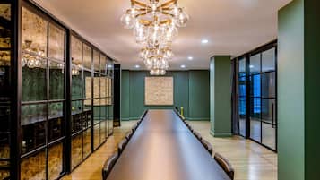 A long conference table in a modern room with a chandelier, large windows, and a green accent wall.