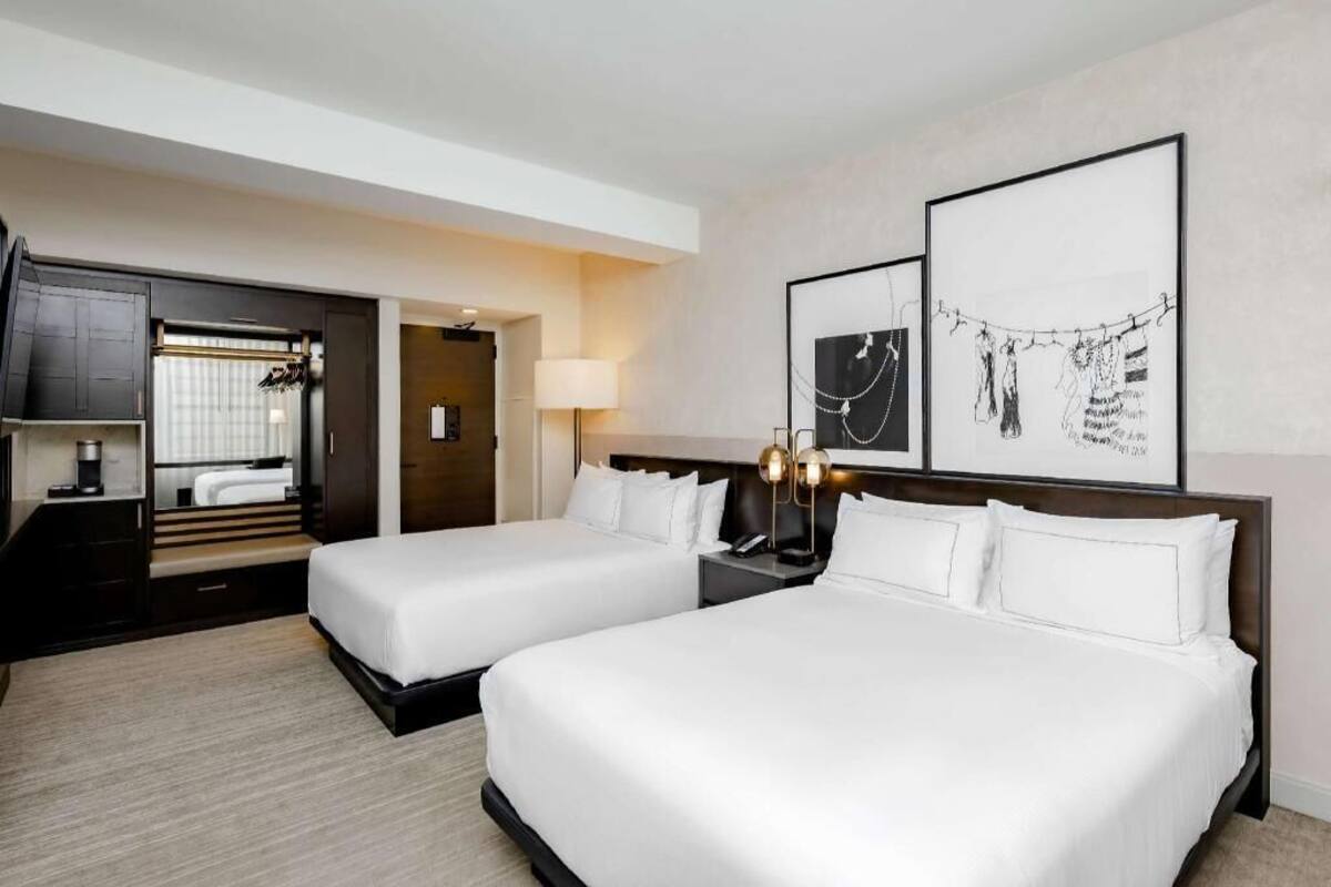 A hotel room with two beds, a desk, a lamp, and artwork on the wall.