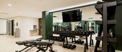 A gym with exercise equipment, a bench, and a television on the wall.