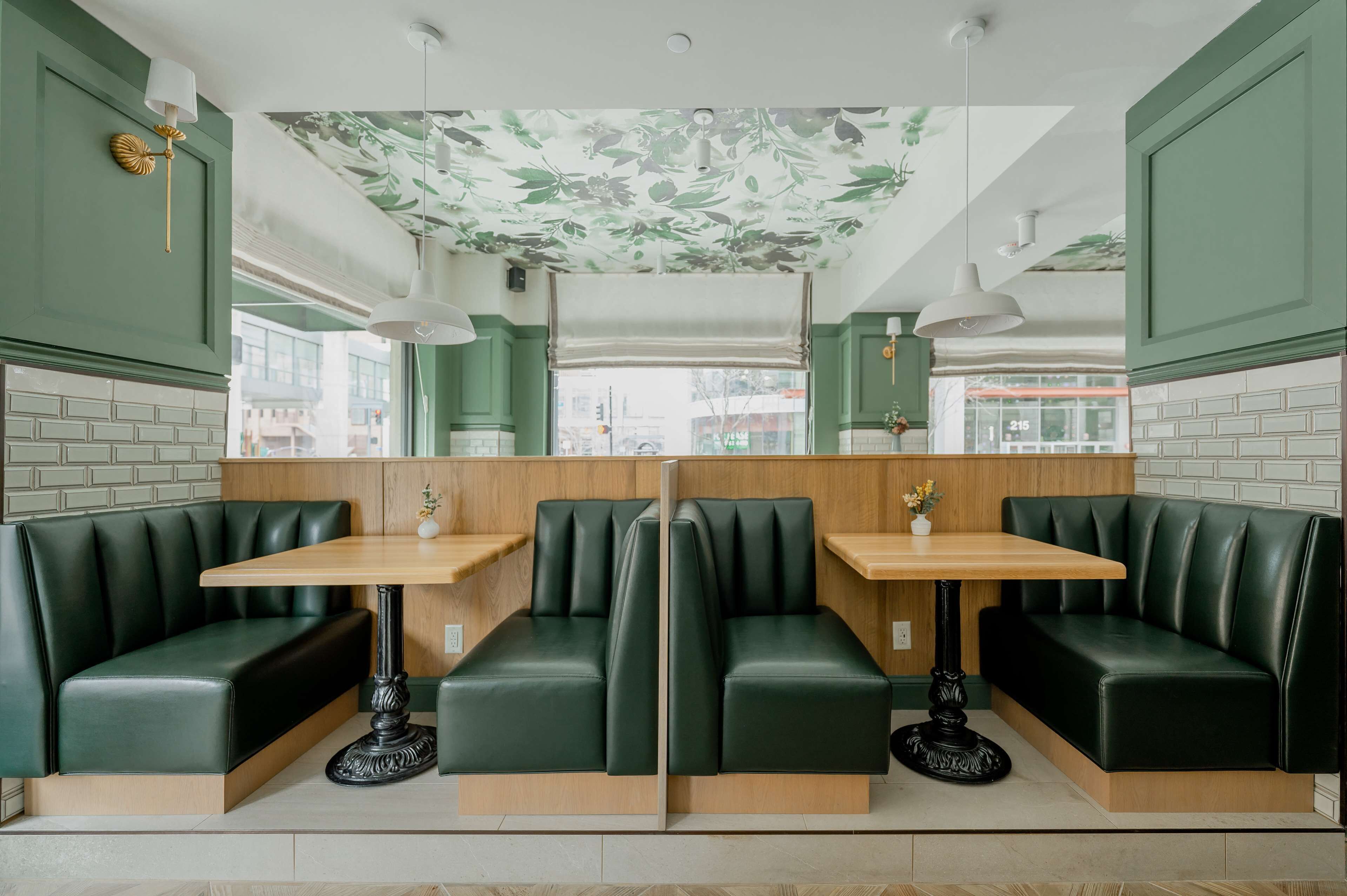 Un restaurante con asientos tapizados en verde, mesas de madera y un techo decorado con motivos florales.