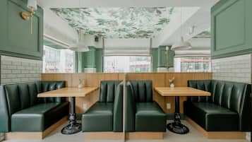 Un restaurante con asientos tapizados en verde, mesas de madera y un techo decorado con motivos florales.