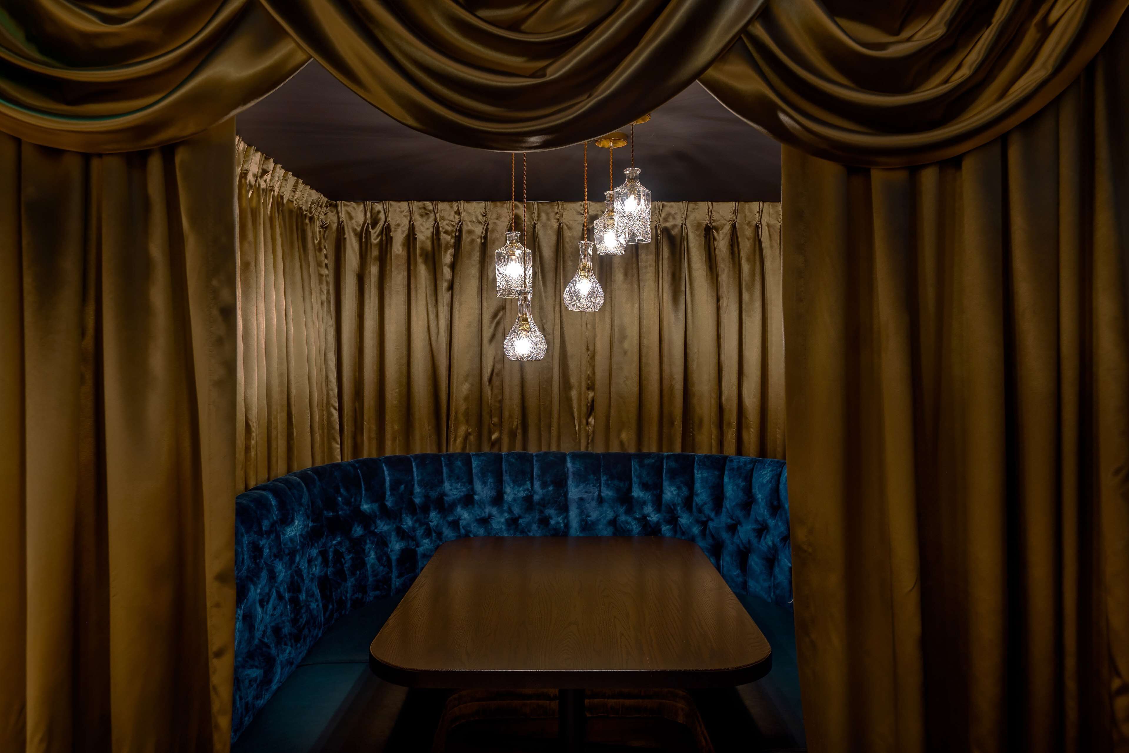 A room with a curved blue velvet bench, a wooden table, and hanging crystal light fixtures.