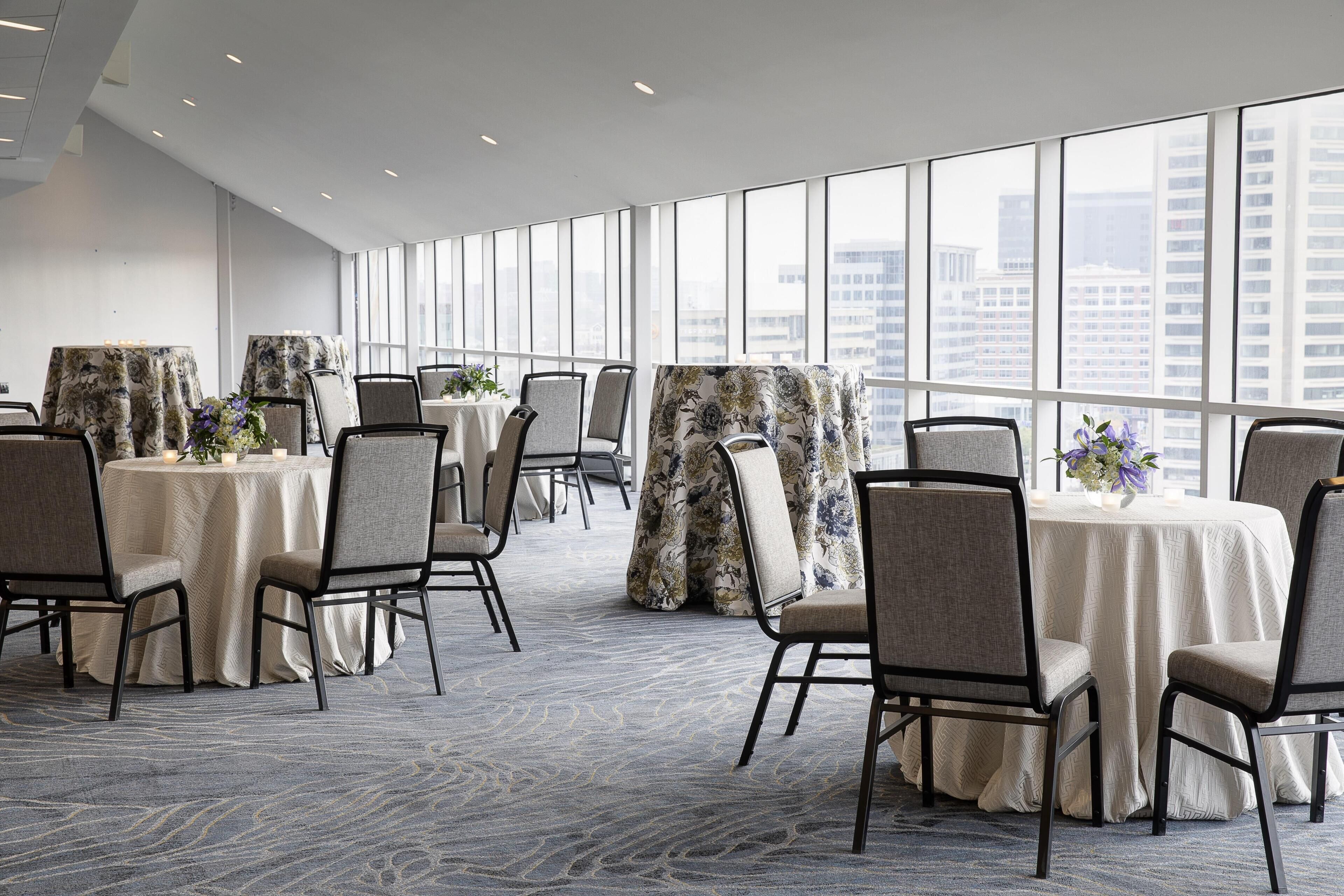 A conference room with round tables, chairs, and large windows offering a city view.