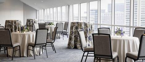 A conference room with round tables, chairs, and large windows offering a city view.
