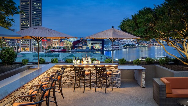 An outdoor bar area with stone seating, umbrellas, and a view of a marina. - Hyatt Regency Baltimore Inner Harbor (Baltimore)