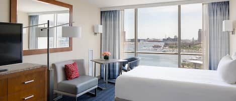 A hotel room with a bed, a desk, a chair, a TV, and a large window with a city view.