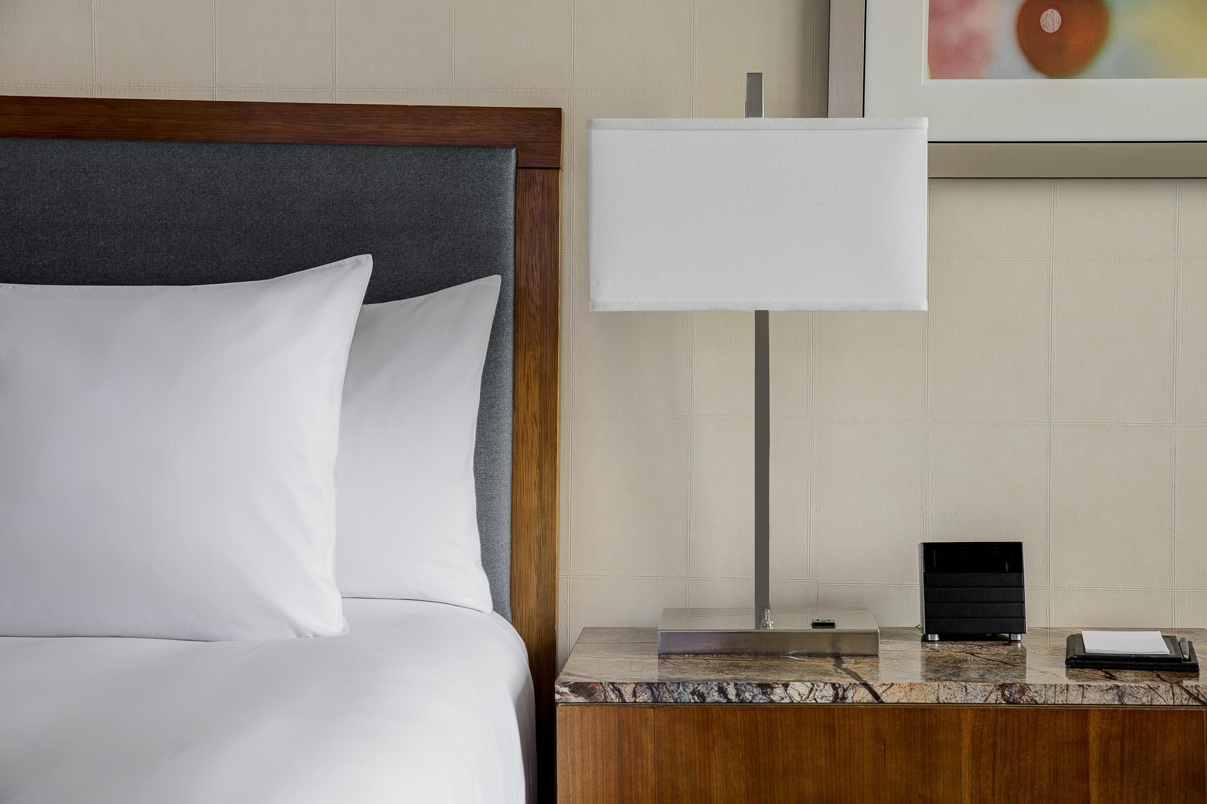 A hotel room with a bed, a nightstand, a lamp, a mirror, and a framed picture on the wall.