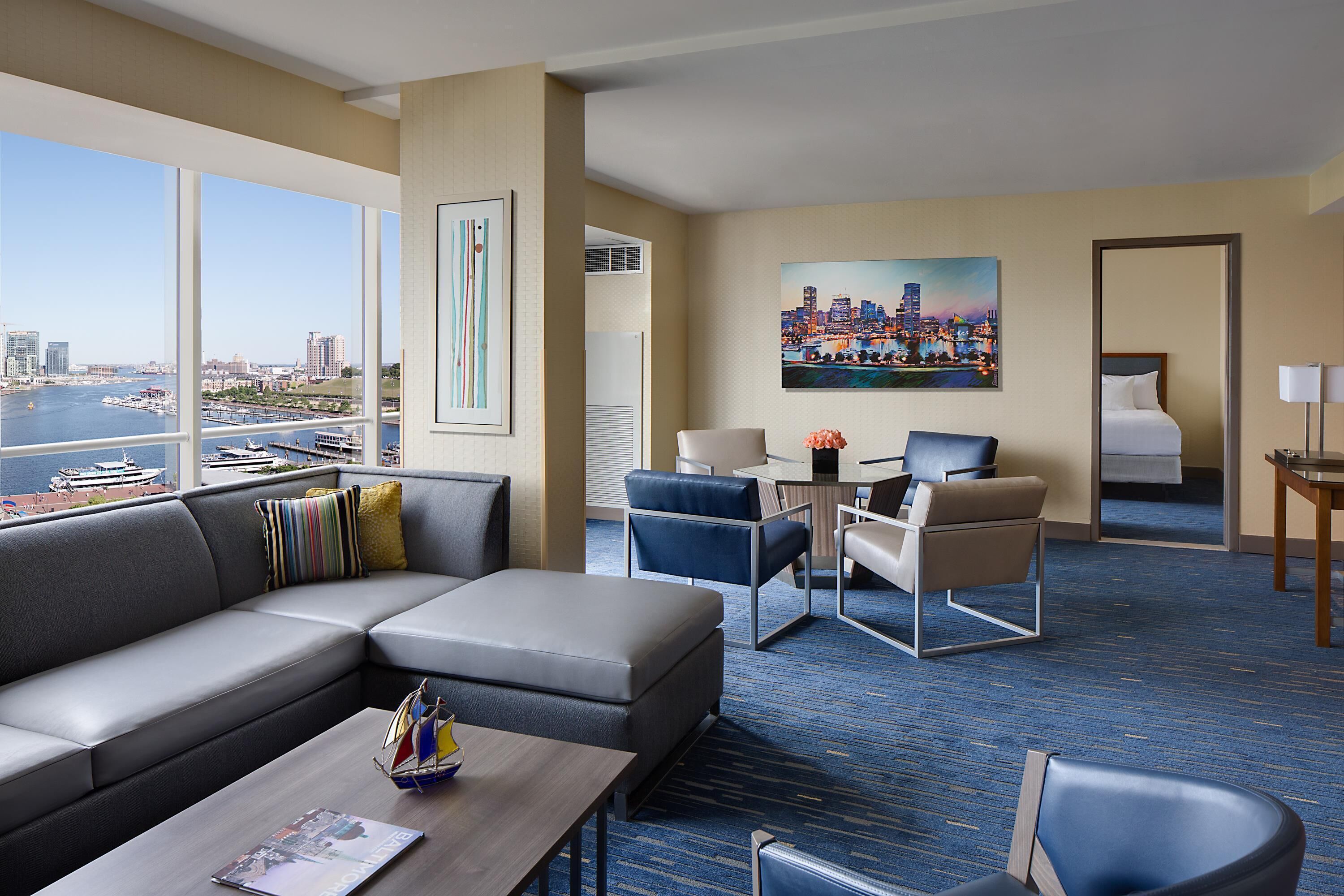 A hotel room with a large window, a sofa, a dining table, and a bed.