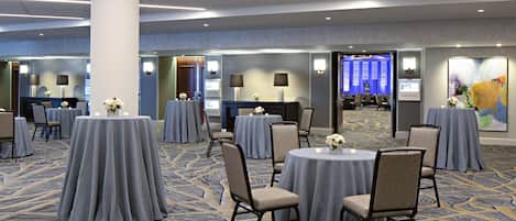 A conference room with round tables, chairs, and a carpeted floor.