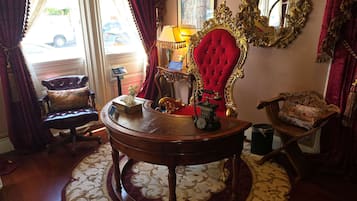 Una habitación con una mesa redonda de madera, una silla tapizada en rojo y una máquina de escribir antigua.