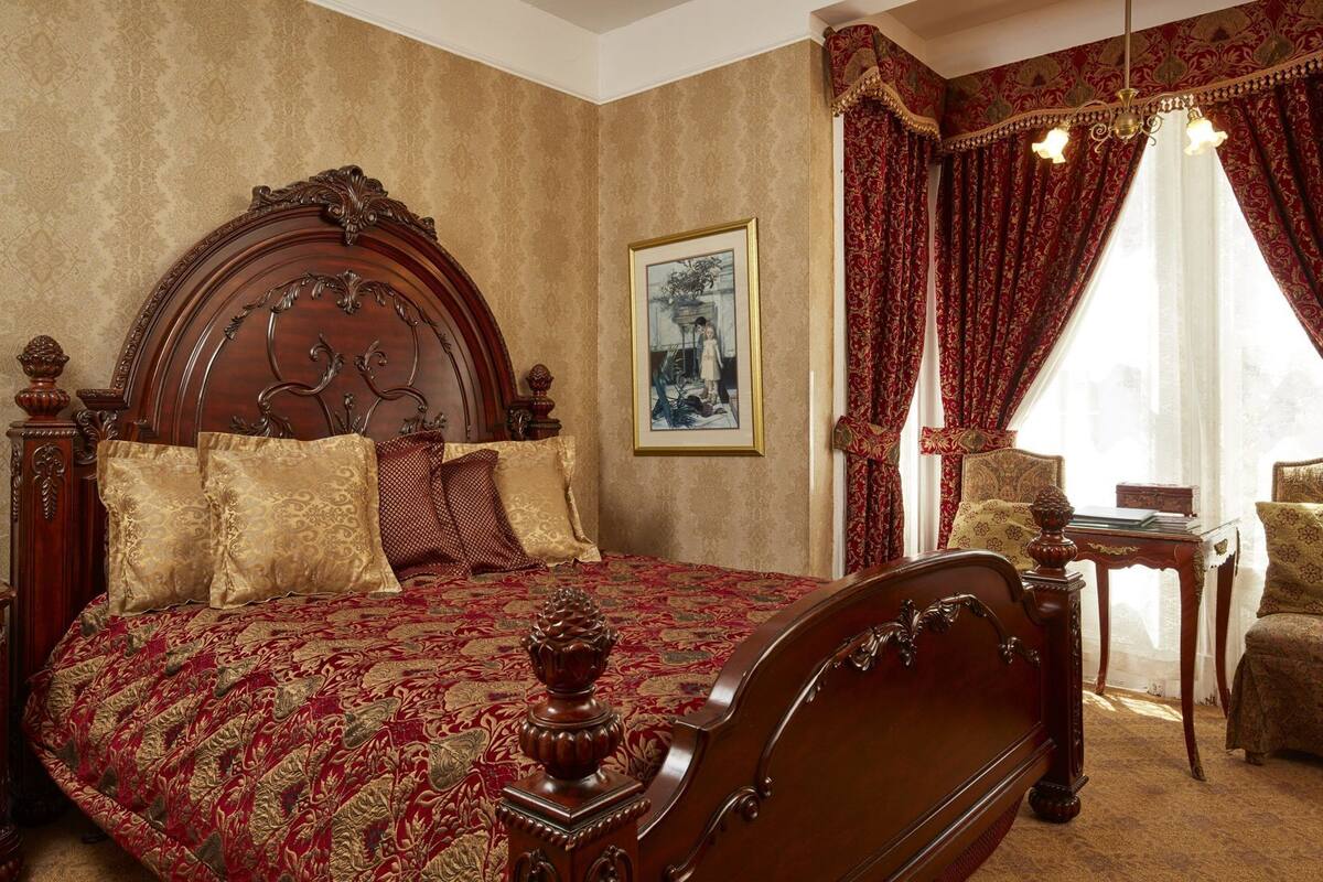 A classic room with a large bed, ornate headboard, and a framed picture on the wall.
