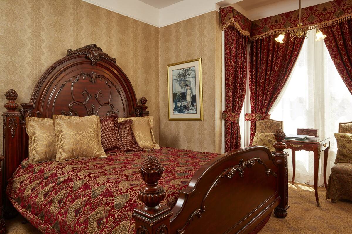 A classic bedroom with a large bed, ornate headboard, and a framed picture on the wall.