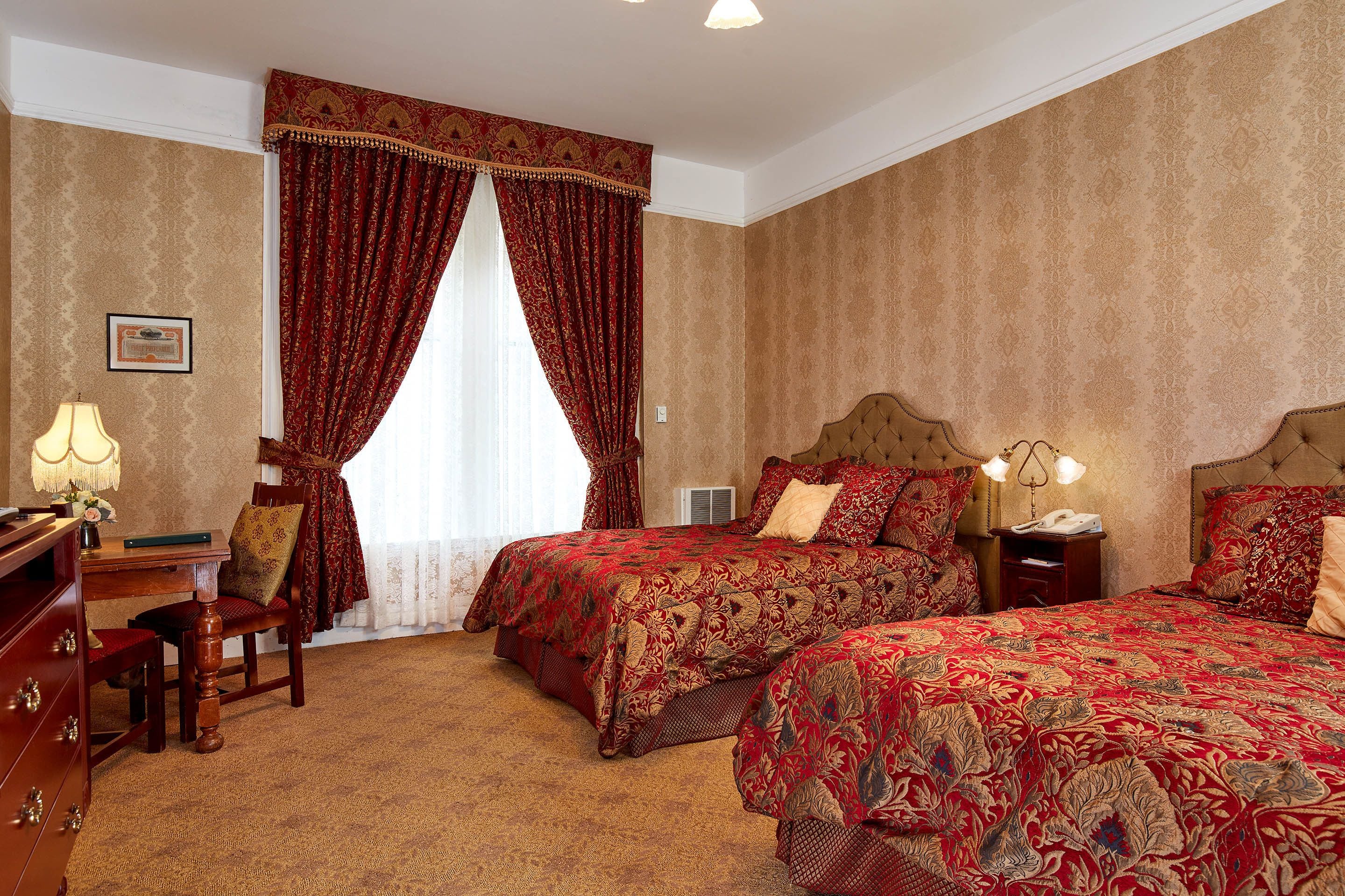 Una habitación de hotel con dos camas, un escritorio con lámpara, una silla y un aparador.