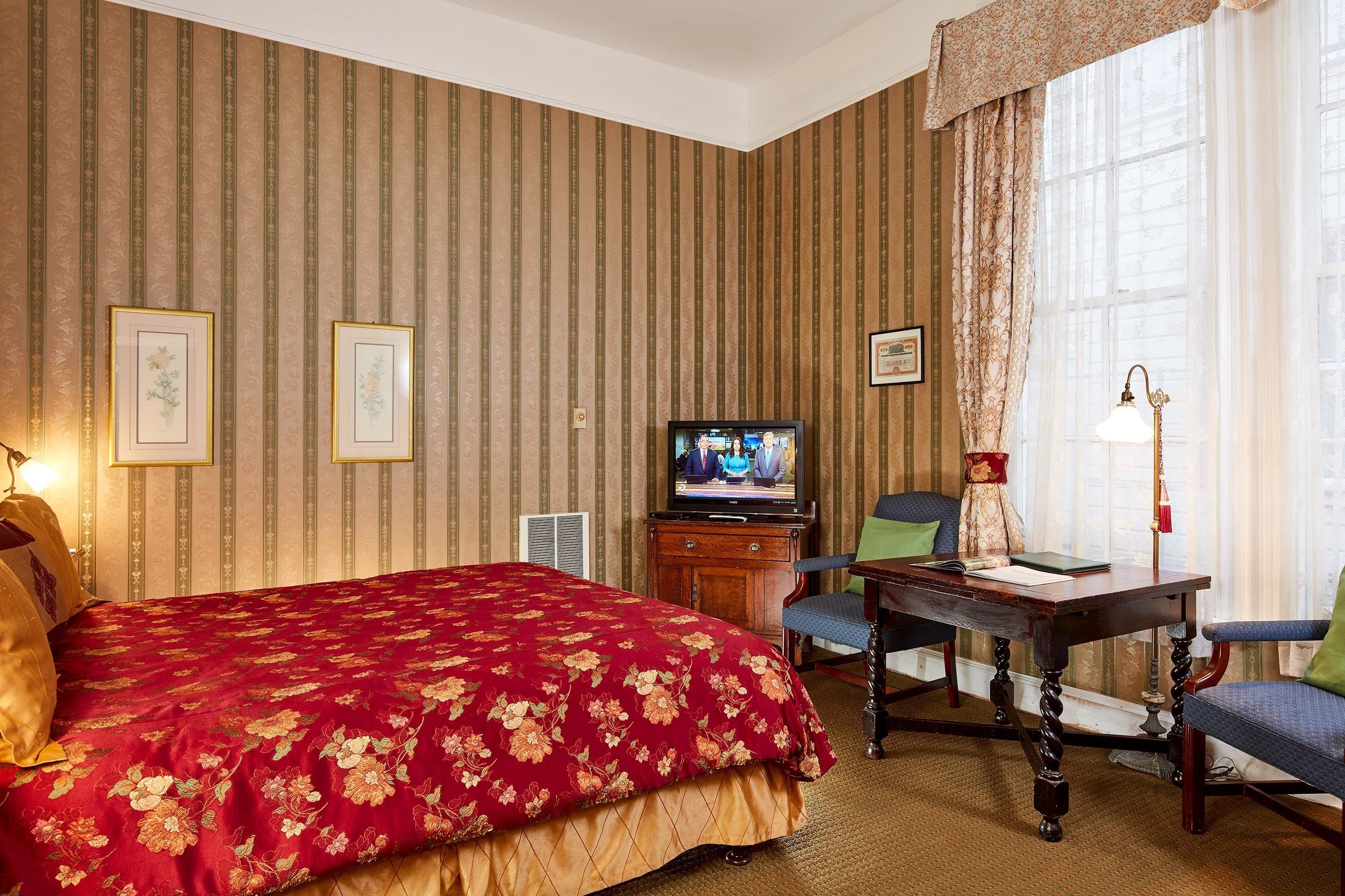 A hotel room with a large bed, a desk, a chair, a television, and a lamp.