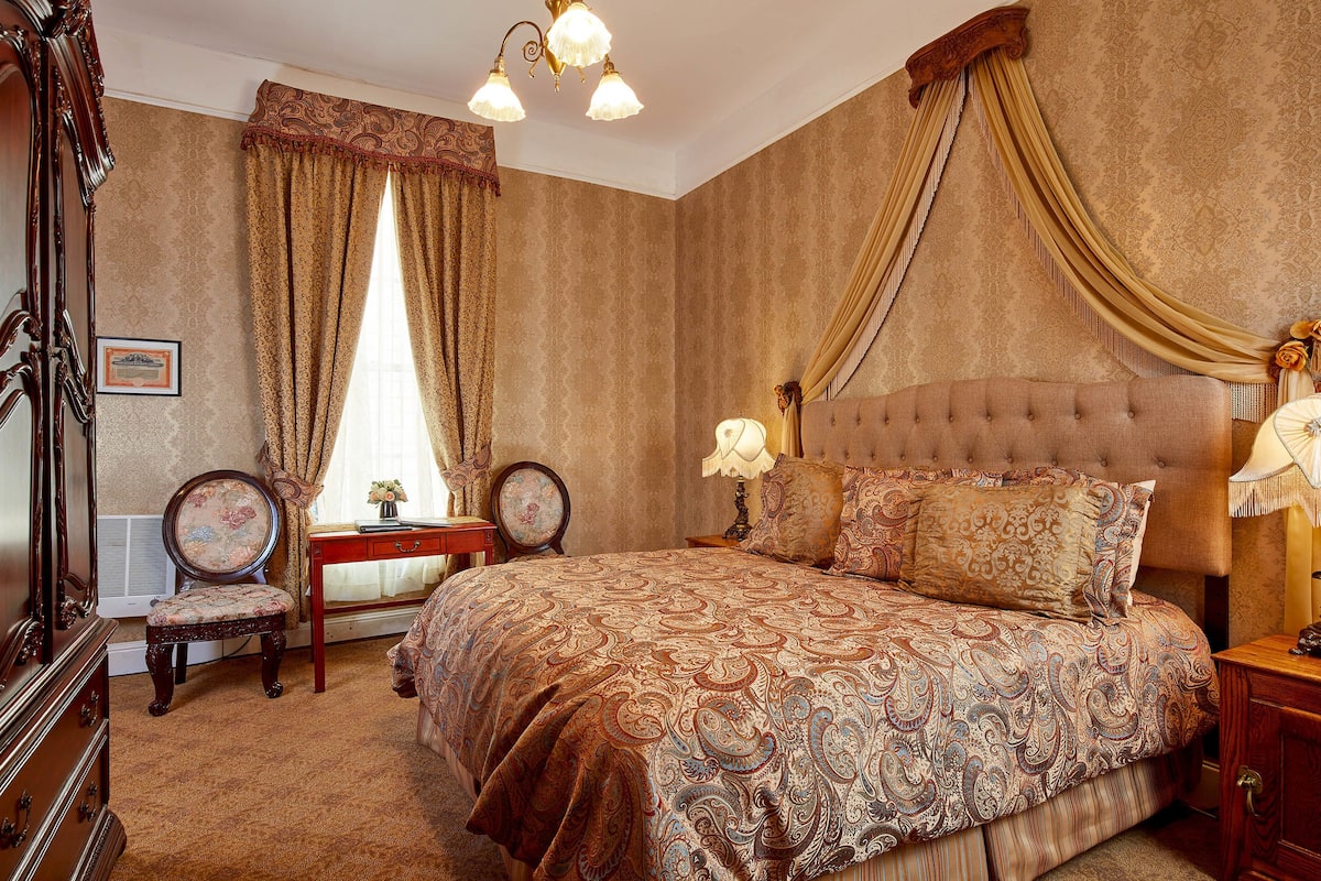 A bedroom with a large bed, a dresser, a vanity, and a chandelier.