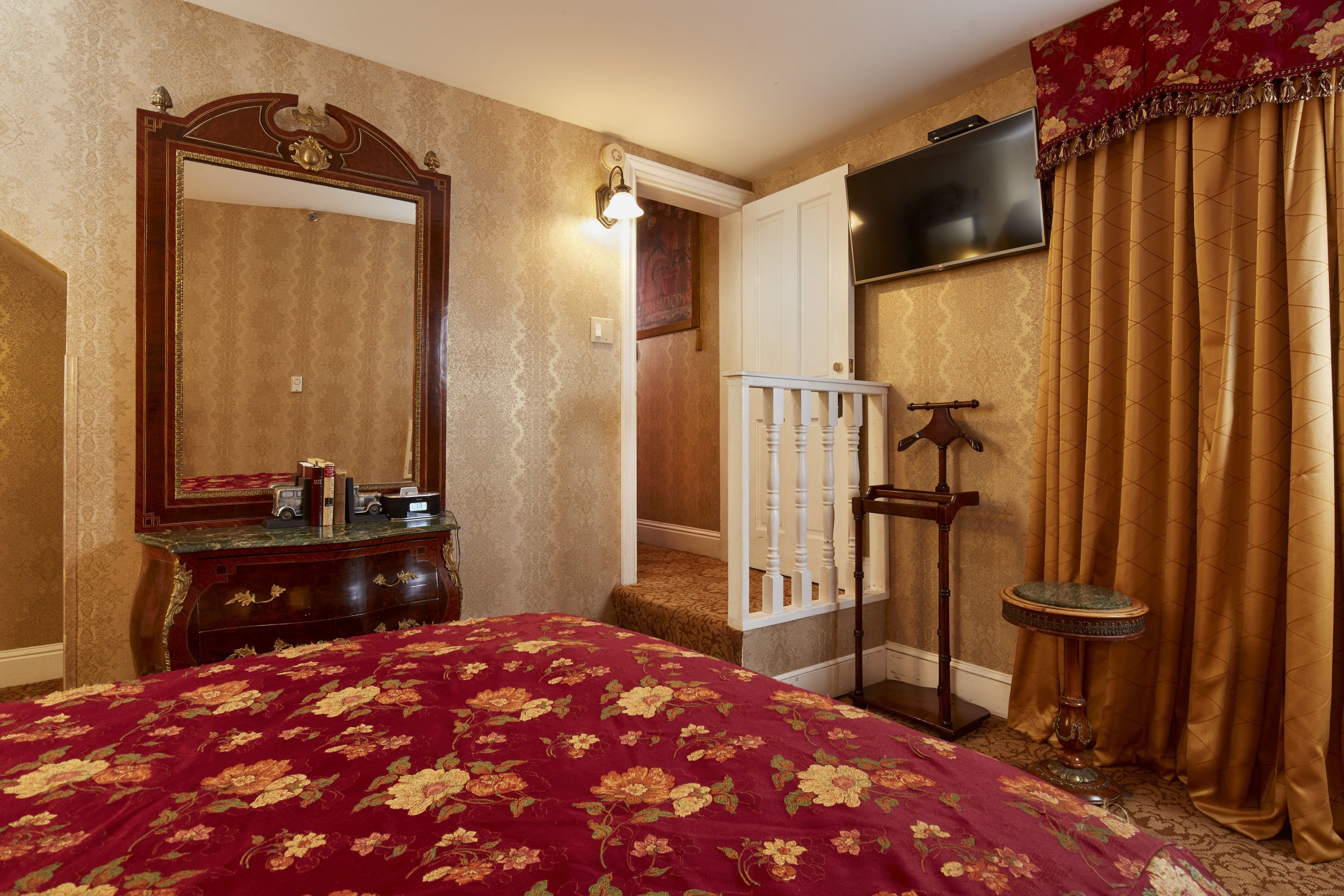 Quarto de hotel com uma cama grande, cômoda, espelho, televisão e escada.