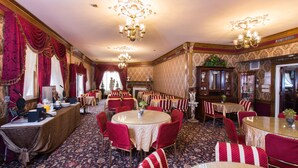 A formal dining room with round tables, red upholstered chairs, and ornate chandeliers. - Queen Anne Hotel (San Francisco)