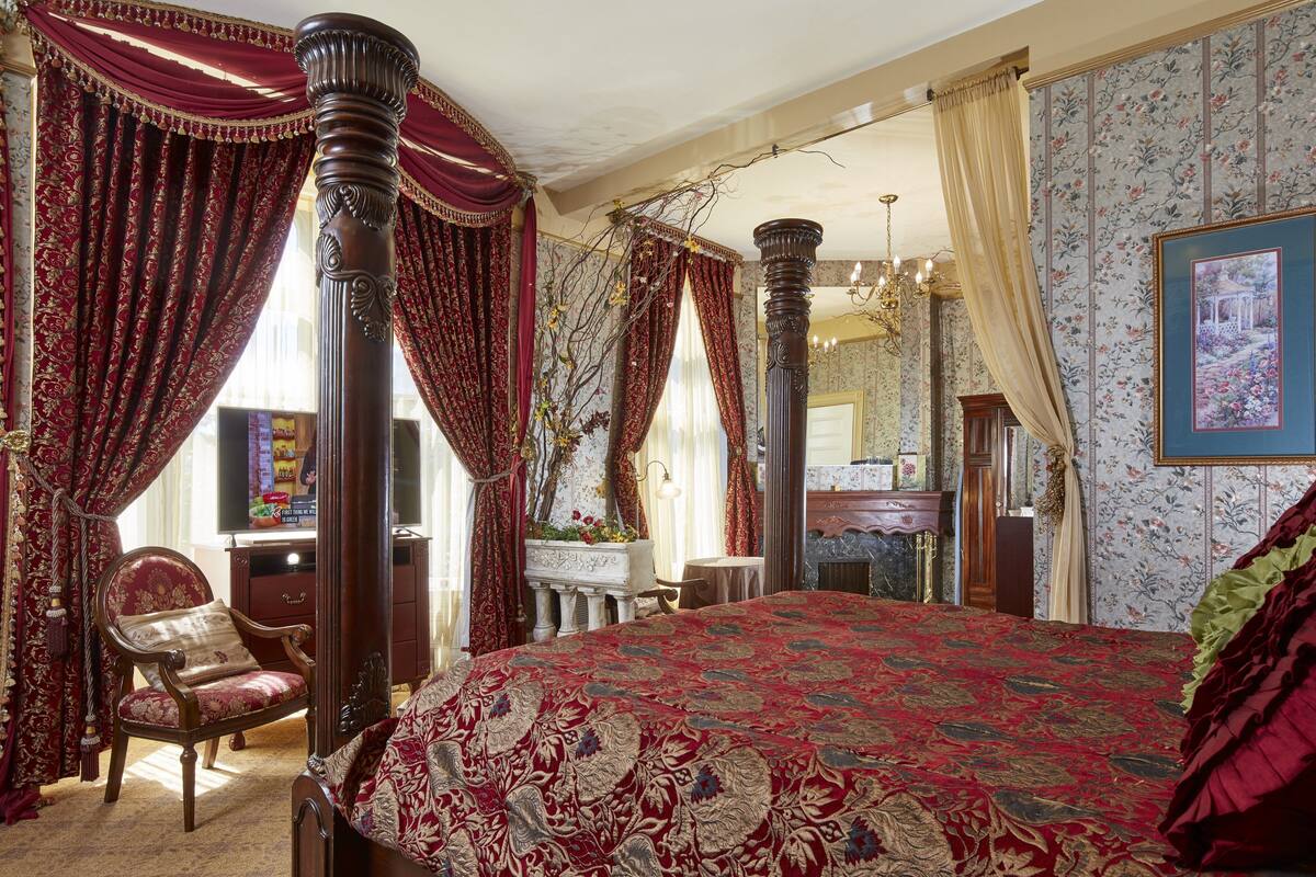 A bedroom with a large bed, a chair, a desk, and a mirror.