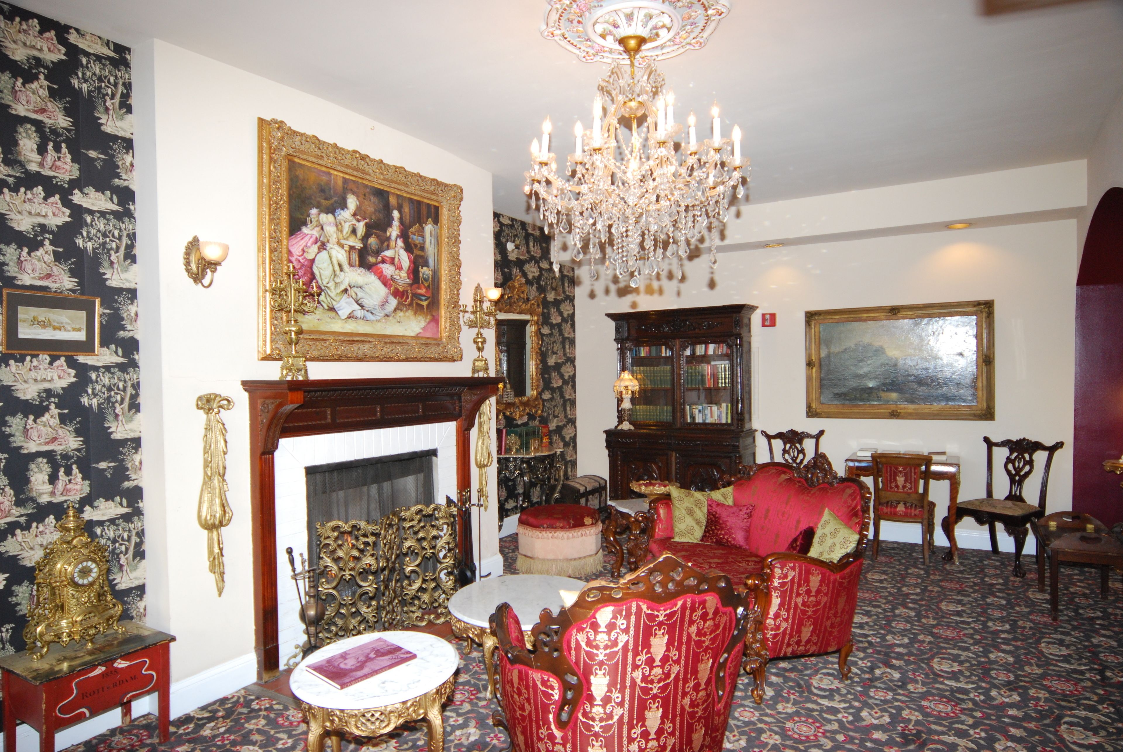Een kamer met een open haard, gedetailleerd meubilair, een kroonluchter en een groot schilderij.